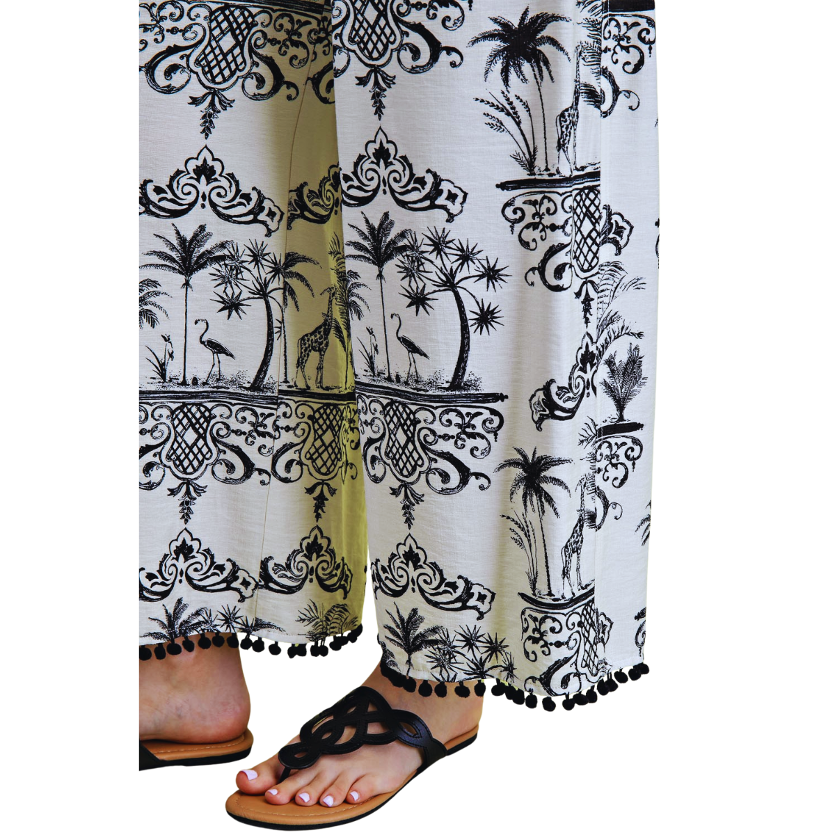 A person models the FASHION GO Toile Print 2 piece Set, featuring relaxed fit pants with a black and white tropical design and black sandals, against a white background.