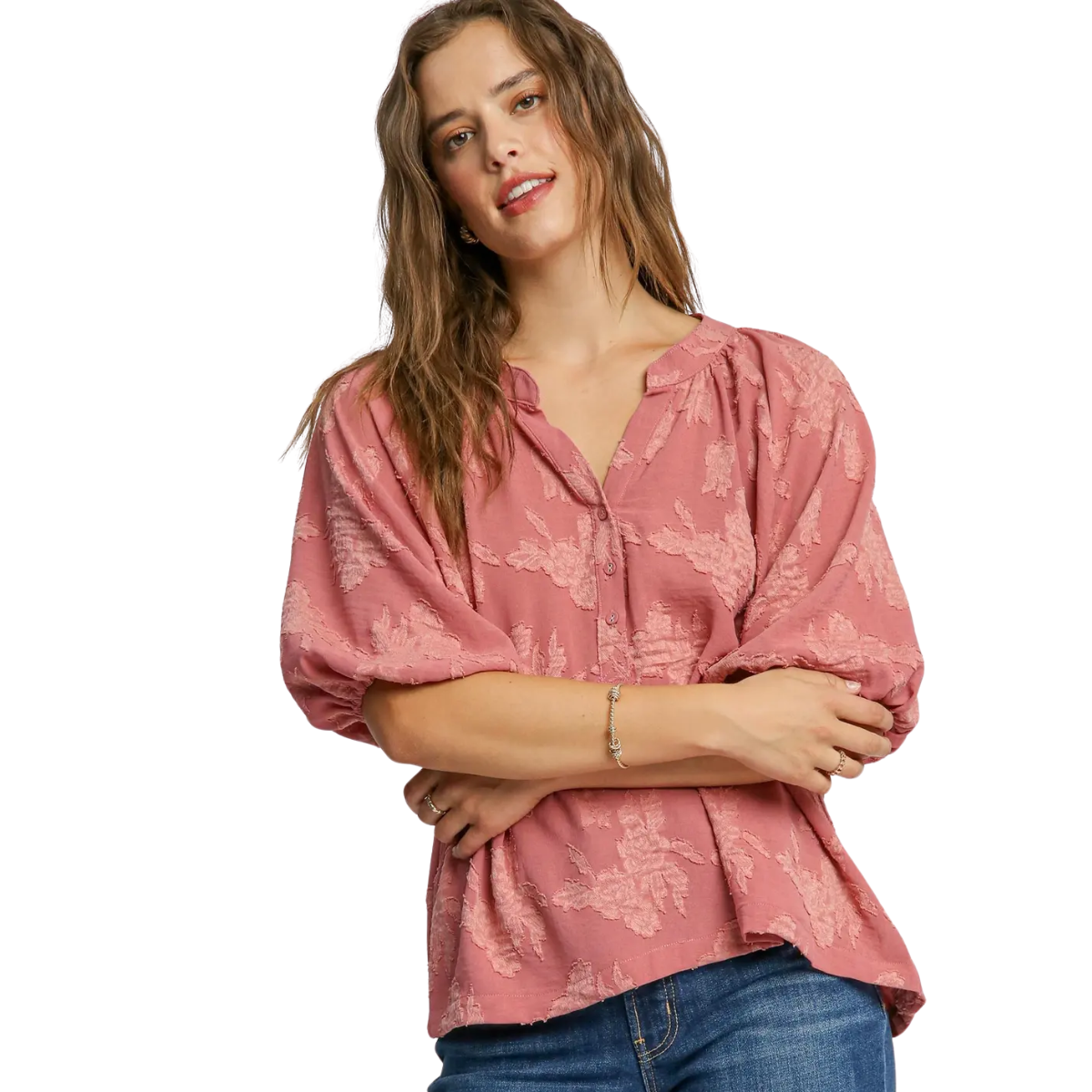 A woman with long brown hair models the Umgee Textured Floral Puff Sleeve Blouse in rose, paired with blue jeans, standing against a white background.