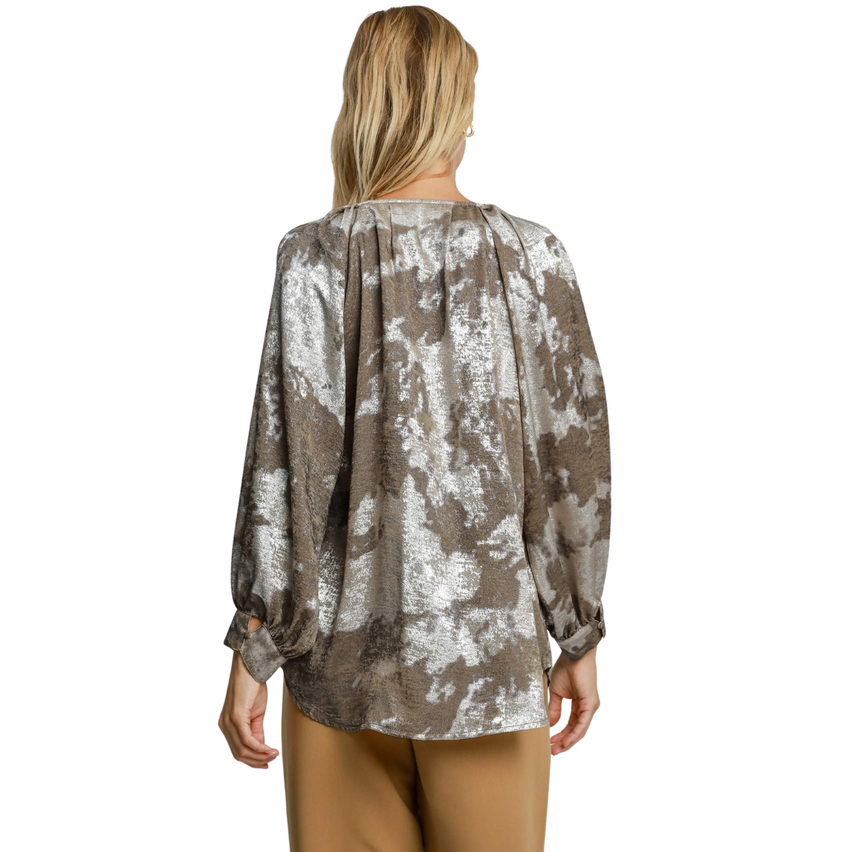 A woman stands facing away, wearing the Umgee Metallic V-notched Collar Blouse with bubble sleeves and a brown and white abstract pattern, paired with tan pants.