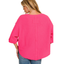 A woman with blonde hair wears the Zenana Double Knit Exposed Seam Curved Hem Top in bright pink with three-quarter sleeves and blue jeans, shown from the back against a white background.