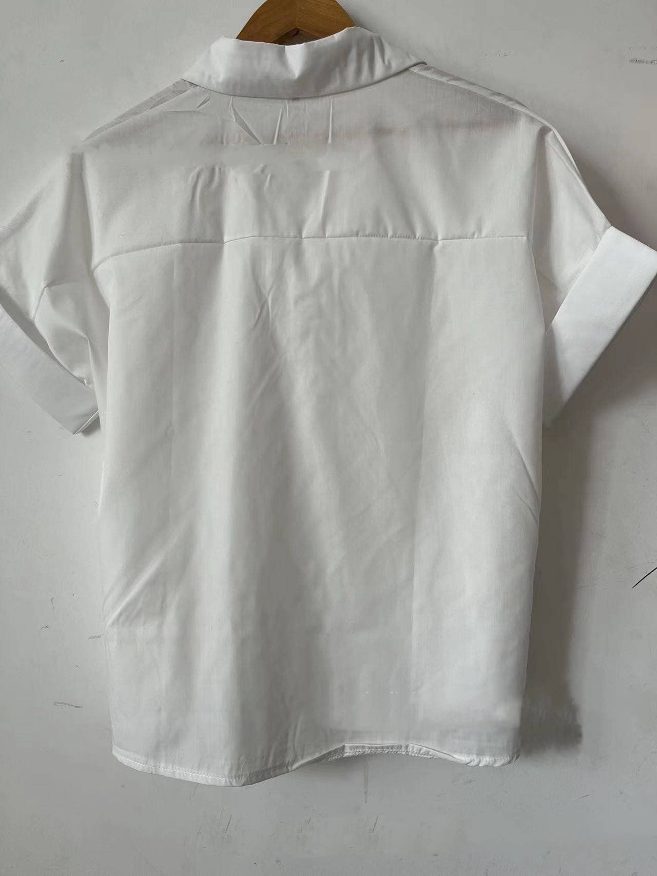 The White Relaxed Short Sleeve Blouse by Rosa Clothing exudes chic style, shown from the back on a hanger against a plain white wall for a classic look.