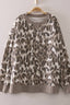 The Leopard Printed Crew Neck Sweatshirt by very J features a stylish gray and beige leopard print, long sleeves, and ribbed cuffs, hem, and neckline. Displayed on a wooden hanger against a light-colored wall, its relaxed fit offers effortless style.