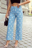 A person stands on a cobblestone street in 1 the Woman Polka Dot Frayed Edge Wide Leg High Waist Jeans, a black crop top, white heeled sandals, and a small black handbag for a chic women’s statement denim look.