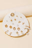 The Anarchy Street Mixed Styles Stud Earrings Set features assorted gold and pearl studs, floral, heart, and hoop designs neatly arranged on a round white display card.