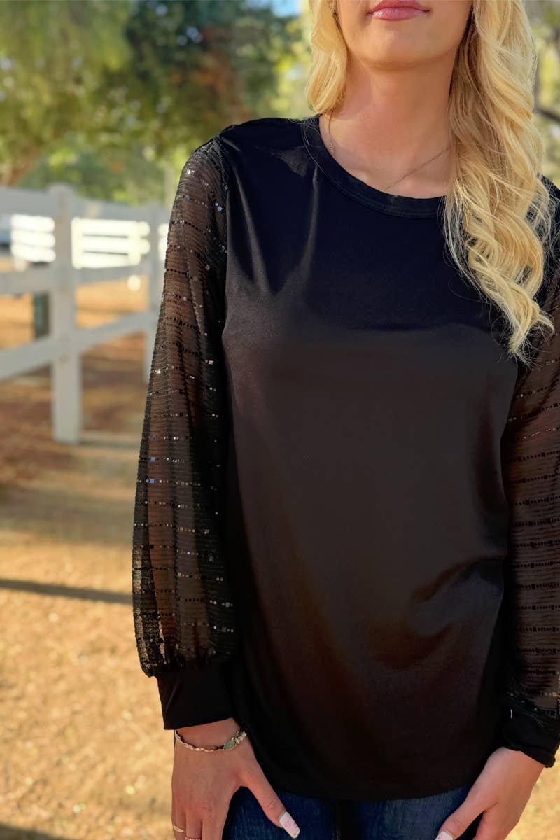 A woman stands outdoors near a white fence wearing the 24-Hrs Fashion Sequin Sleeve Blouse, featuring sheer, textured balloon sleeves.