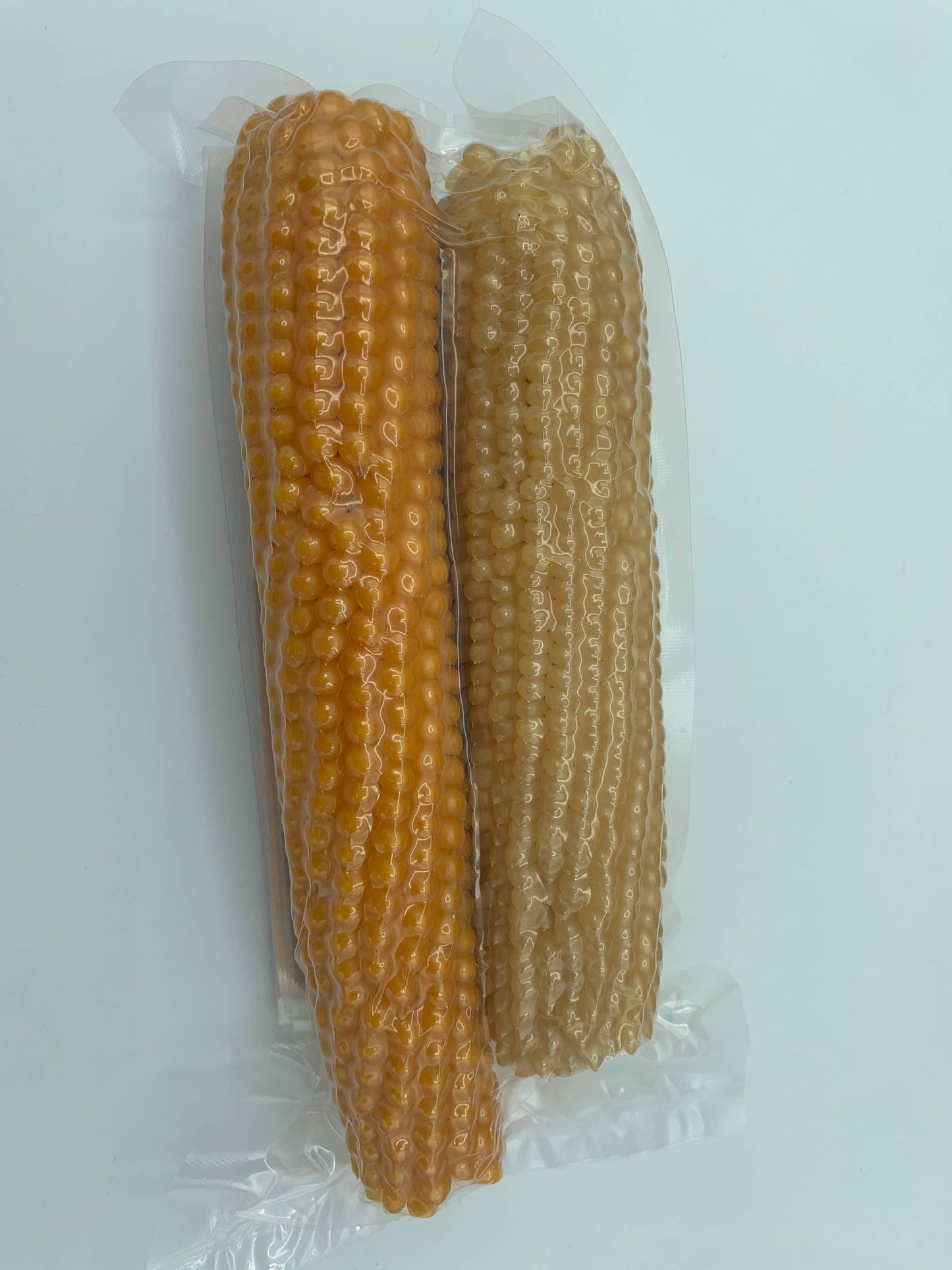 Two whole cobs, one orange and one light brown, are sealed side by side in a clear pouch. Amish Country Popcorn's Twin Microwave Popcorn Cobs are perfect for easy popping. Set against a plain white background.