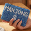 A hand holds the Blue Mahjong Money Seed Beaded Coin Purse by Anarchy Street, featuring white seed bead accents, a zipper, and “MAHJONG $” spelled out in bold beaded letters.