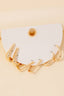 The Anarchy Street Mixed Long Oval Hinge Hoop Earrings Set showcases five pairs of gold hoops with an elegant oval hinge design on a white textured semicircular card with a central hole, displayed against a beige background.