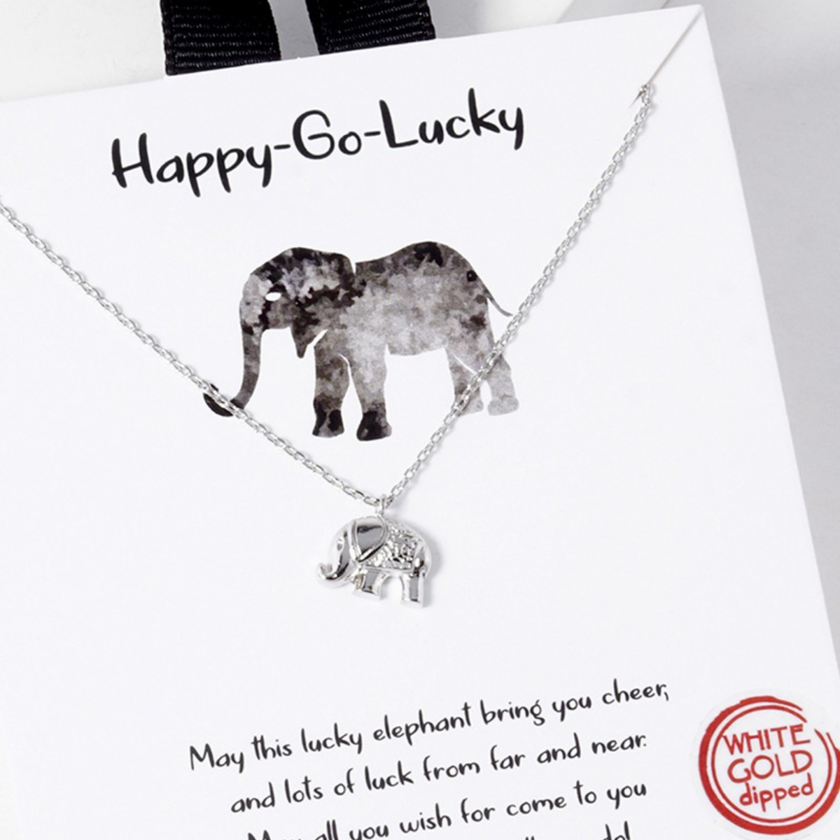 A Tiny Elephant Pendant necklace by SPECIAL EFFECTS, presented on a card adorned with an illustrated elephant and the text "Happy-Go-Lucky" at the top. The necklace features a delicate 16" silver chain and an elegant "White Gold Dipped" stamp.