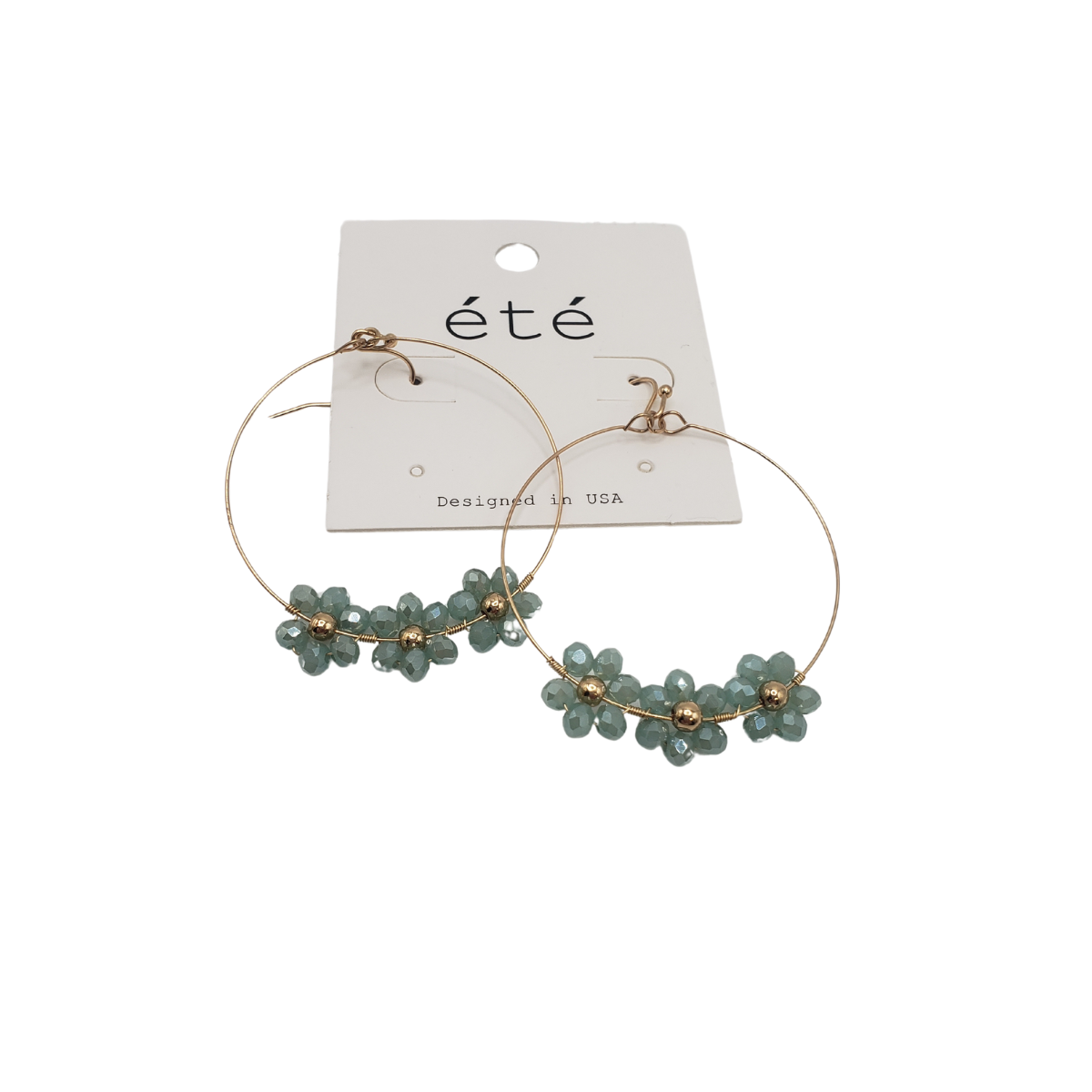 Crystal Flower Hoop Earrings by SPECIAL EFFECTS feature gold hoops with blue-green flower beads and sparkling crystals, attached to a white card labeled "été," offering an elegant and versatile timeless design.