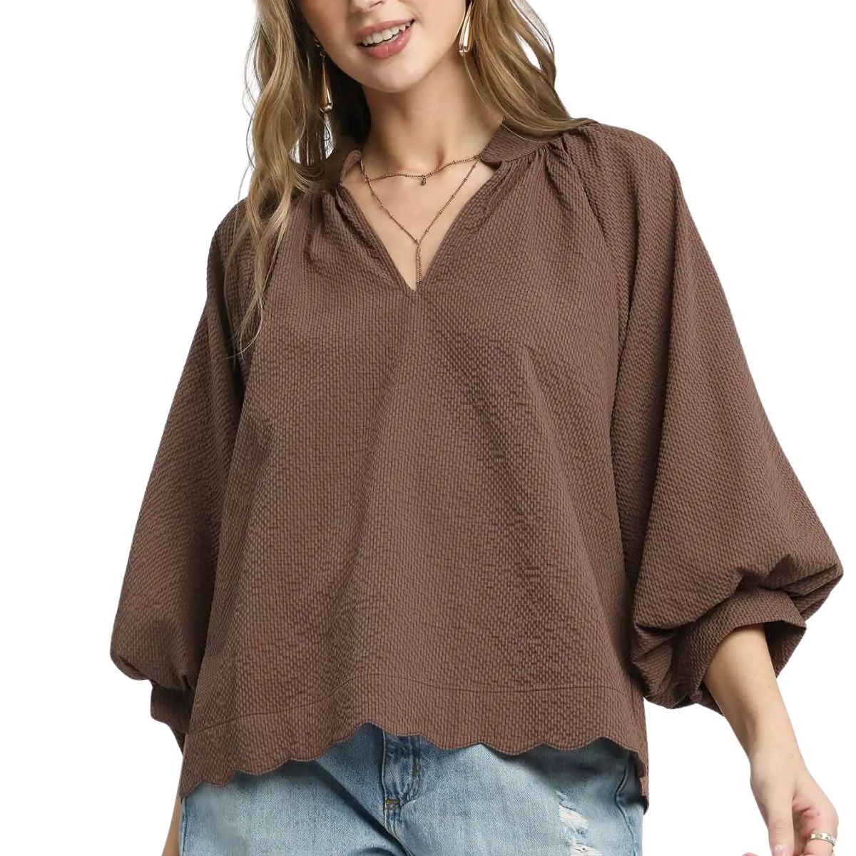 A person wearing the Umgee Split V Neck Top with Balloon Sleeves in brown, featuring textured fabric and a scalloped hem, paired with light blue distressed jeans.