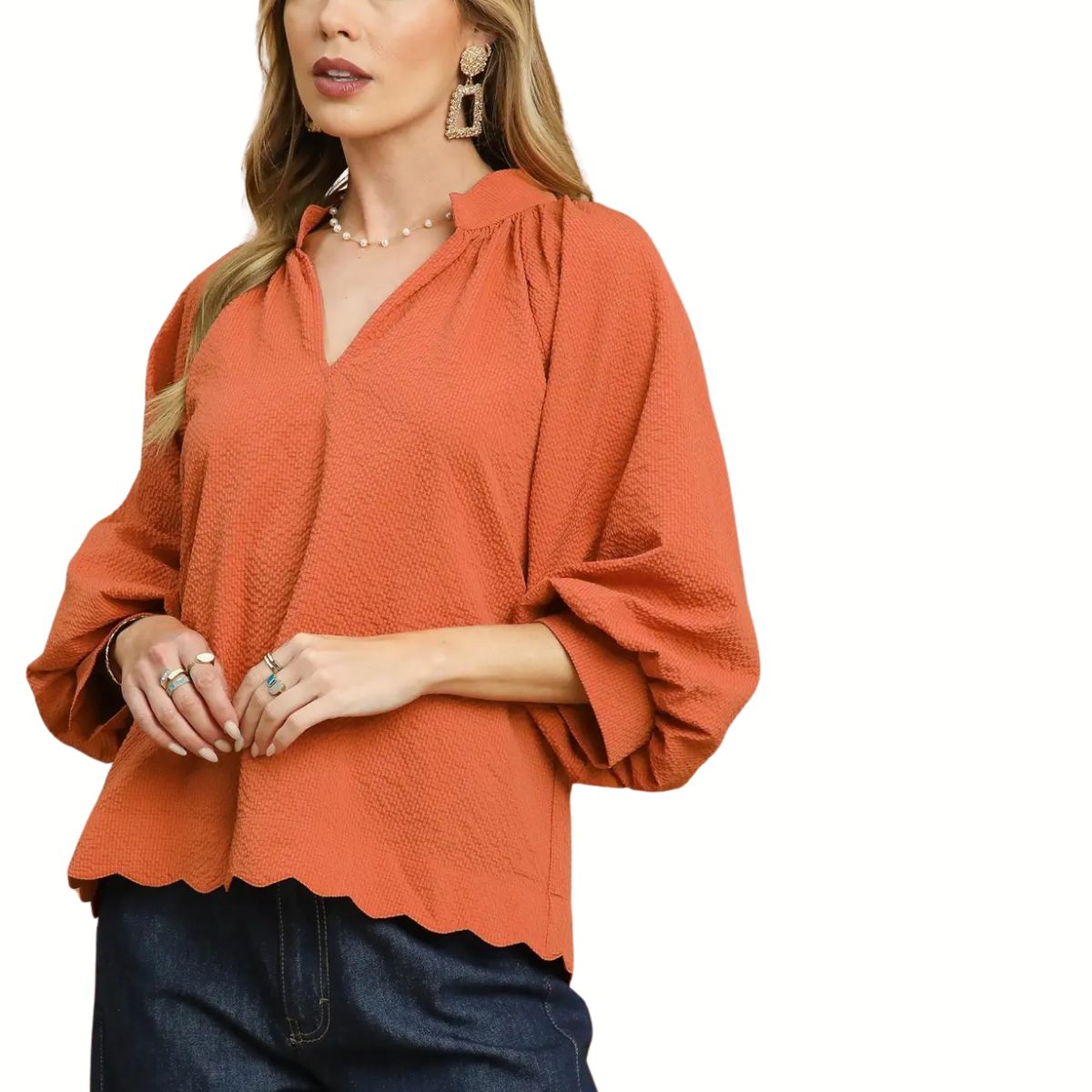 A woman wears the Umgee Split V Neck Top with Balloon Sleeves in burnt orange, featuring textured fabric and a scalloped hem, paired with dark blue jeans.