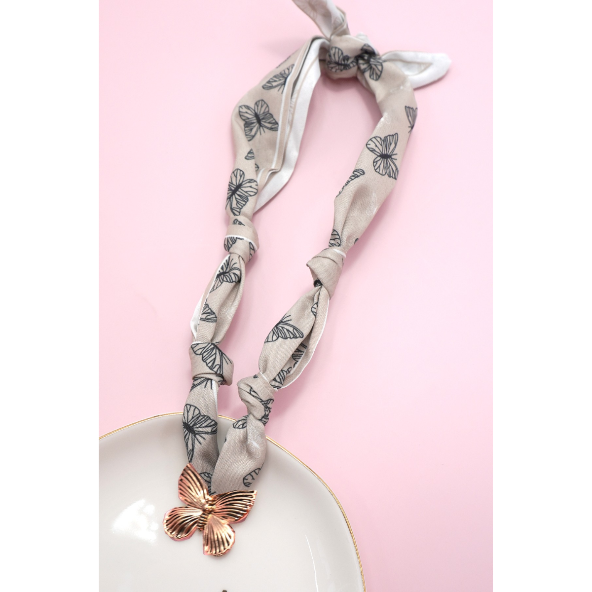 The FASHION GO Handmade Scarf Necklace in assorted colors and patterns is shown on a pink background beside a white plate.