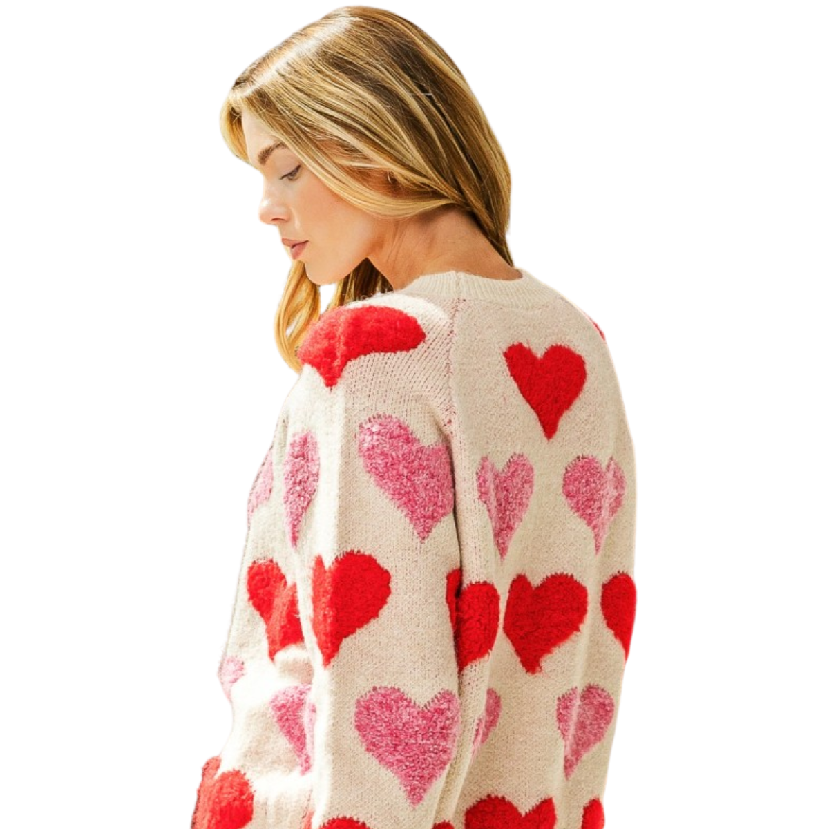 A woman with light brown hair wears the FASHION GO Heart Raglan Sleeve Sweater, featuring red and pink heart patterns, as she looks down against a white background.