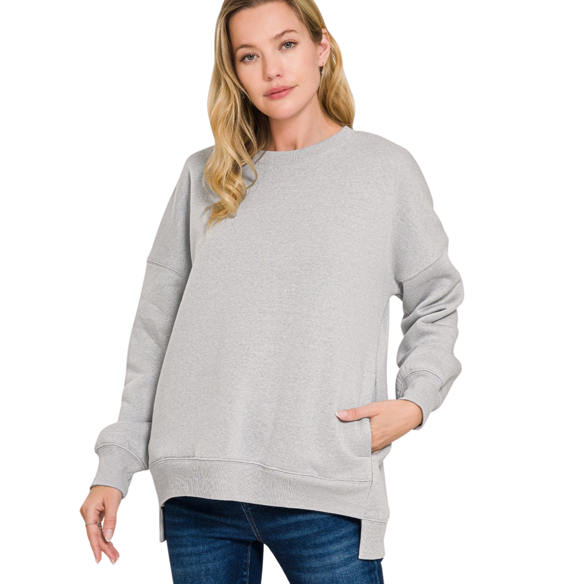 A woman models the Zenana Fleece Hi-Low Hem sweatshirt in light gray with blue jeans, standing with one hand in her pocket against a plain white background.