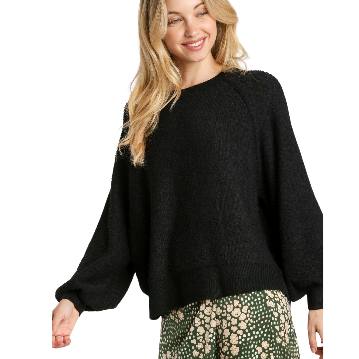 A woman wears the Umgee Puff Sleeve Boat Neck Sweater in black, styled with a green skirt featuring a white floral pattern, against a white background.