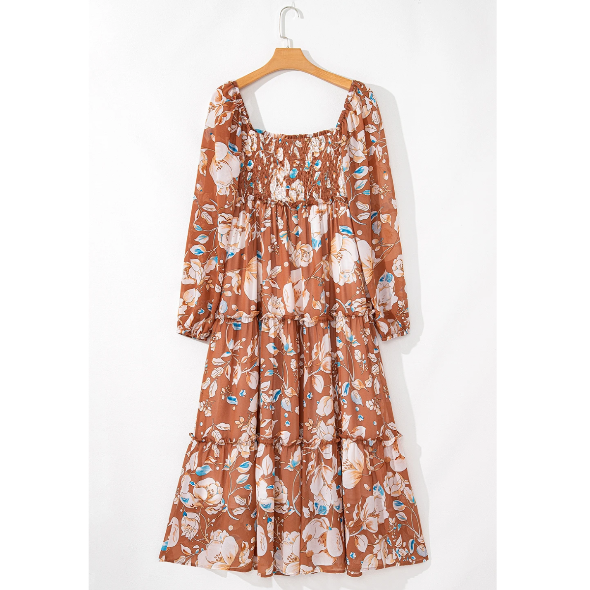 The Shewin Brown Floral Print Shirred Square Neck Maxi Dress with long sleeves elegantly hangs on a wooden hanger against a white wall.