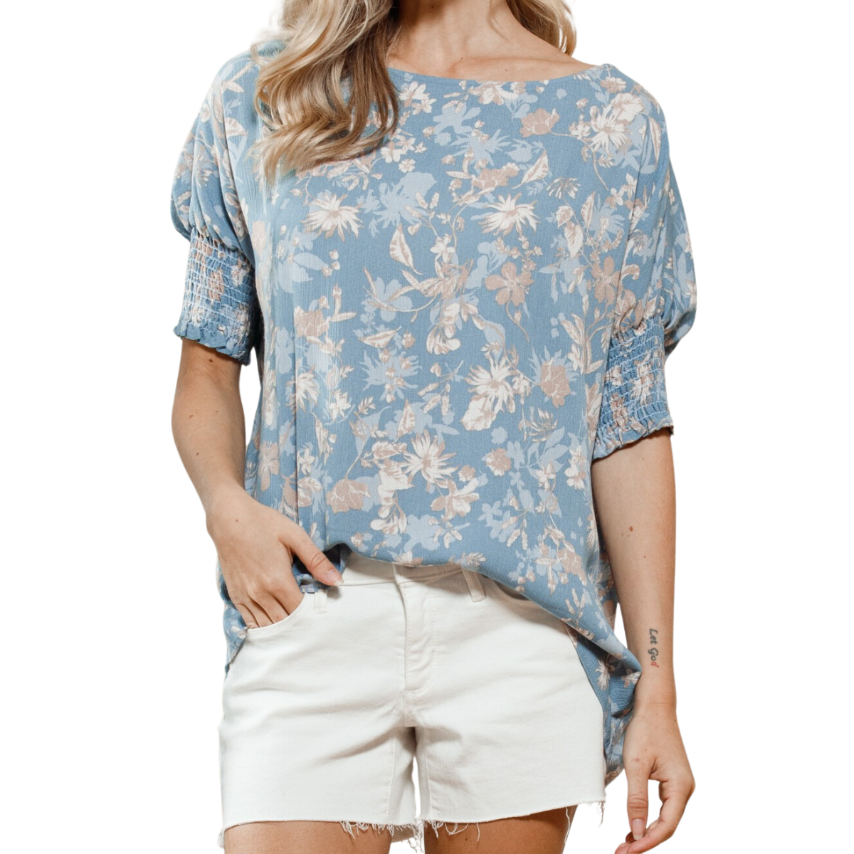A woman confidently models the FASHION GO Floral Printed Boatneck Blouse with short, gathered sleeves, pairing it stylishly with white shorts. Her chic look is completed with one hand casually resting in her pocket.