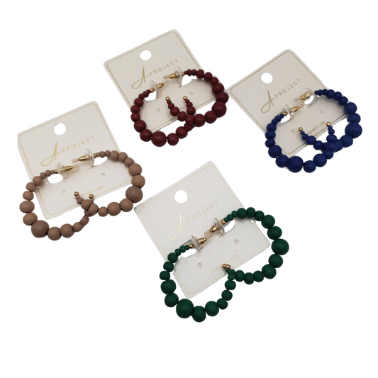 Four pairs of SPECIAL EFFECTS Color Balls Hoop Earrings in beige, maroon, blue, and green are elegantly displayed on cards labeled "Aproject.
