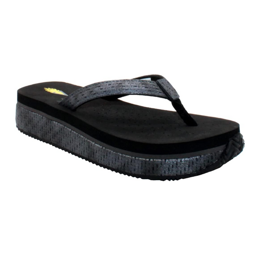 The Untamed Low Wedge Flip Flop in Black Metallic by Volatile from PV Footwear features a single black wedge sandal with a textured platform, ultra-comfort EVA insoles, and metallic tonal gray strap, all set against a white background.