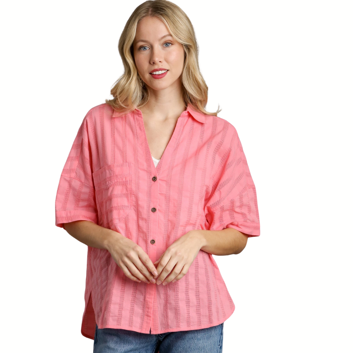 A woman wearing the Umgee Textured Button-Down Blouse in pink over a white V-neck top and blue jeans stands against a white background.