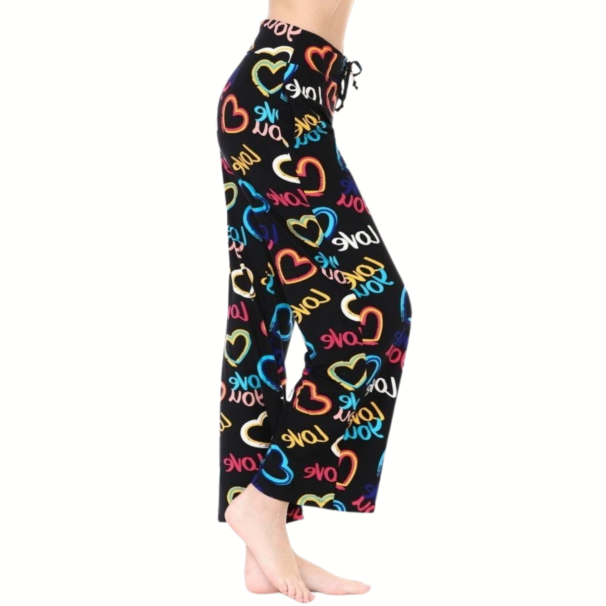 Person wearing FASHION GO Buttery Soft Pajama Pants with Drawstring in black, featuring multicolored heart and "LOVE" prints and an elastic waistband, standing barefoot against a white background.