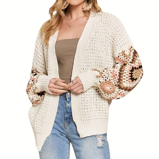 A woman models the Fashiongo Crocket Sleeve Cardigan Sweater, featuring crochet granny square sleeves, over a brown tube top and ripped blue jeans against a white background.