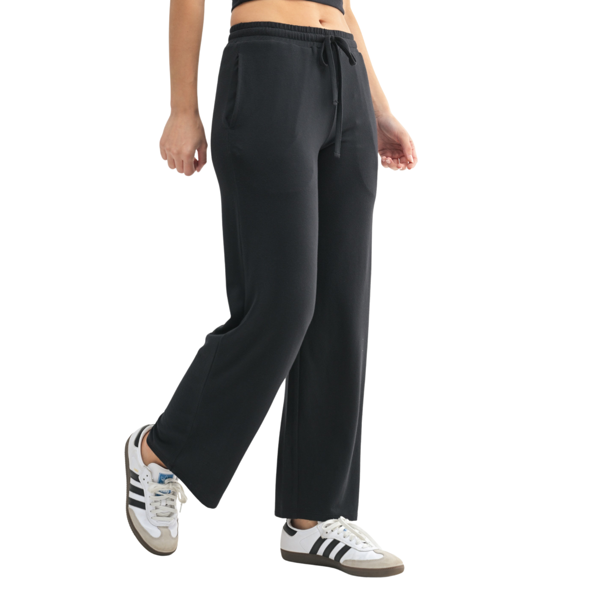 A person wears Fashiongo Brushed Hacci Wide Leg Lounge Pants with a drawstring waist and black-and-white sneakers, standing with one foot slightly raised against a plain white background.