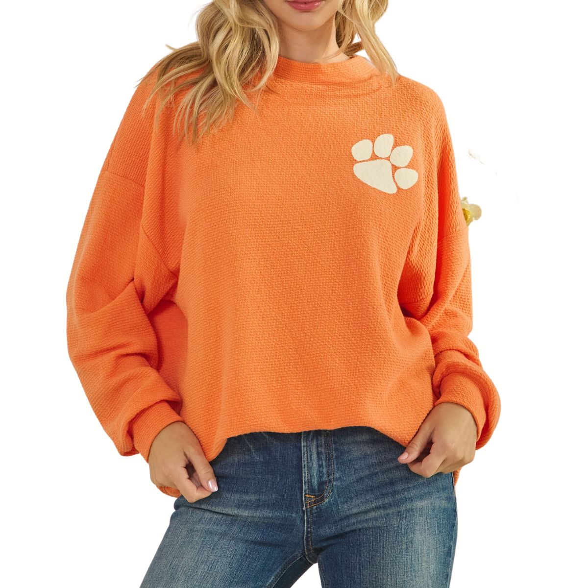 A woman wears the Tres Bien Paw Print TIGERS Cloudy Knit Top in orange with a varsity paw print graphic on the chest, paired with blue jeans.