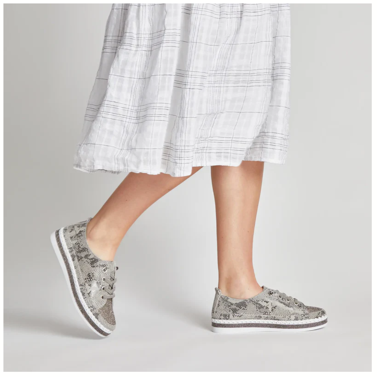 A person wearing a white plaid skirt and BERNIE MEV Jodie Rhinestone Embellished Python Print Sneakers stands against a plain background.