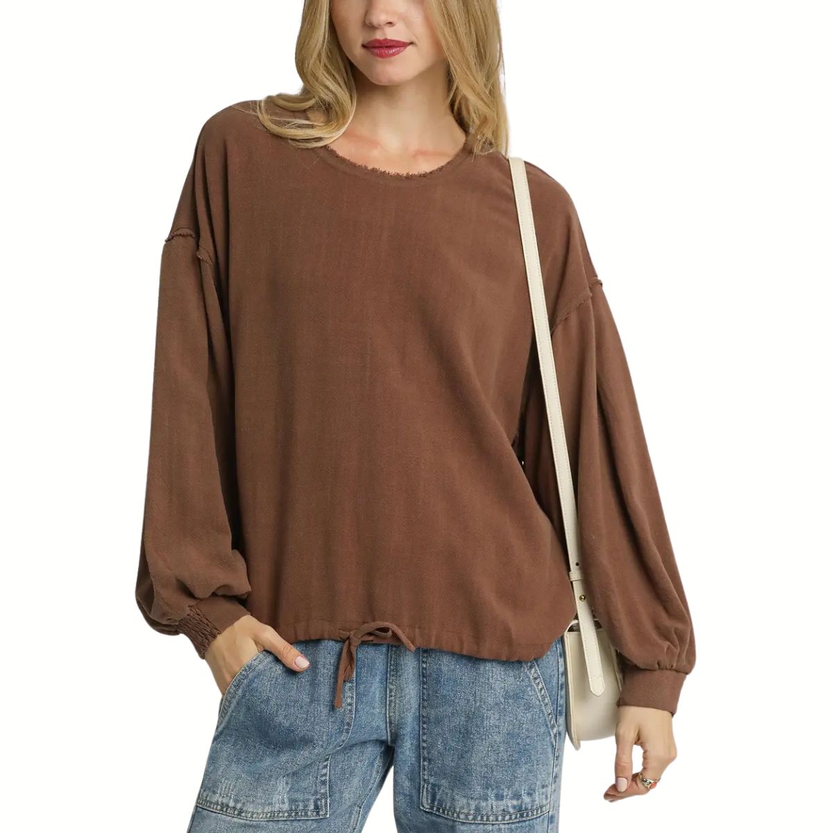 A woman wears the Umgee Linen Long Sleeve Top with Drawstring, paired with light blue jeans and a beige shoulder bag.