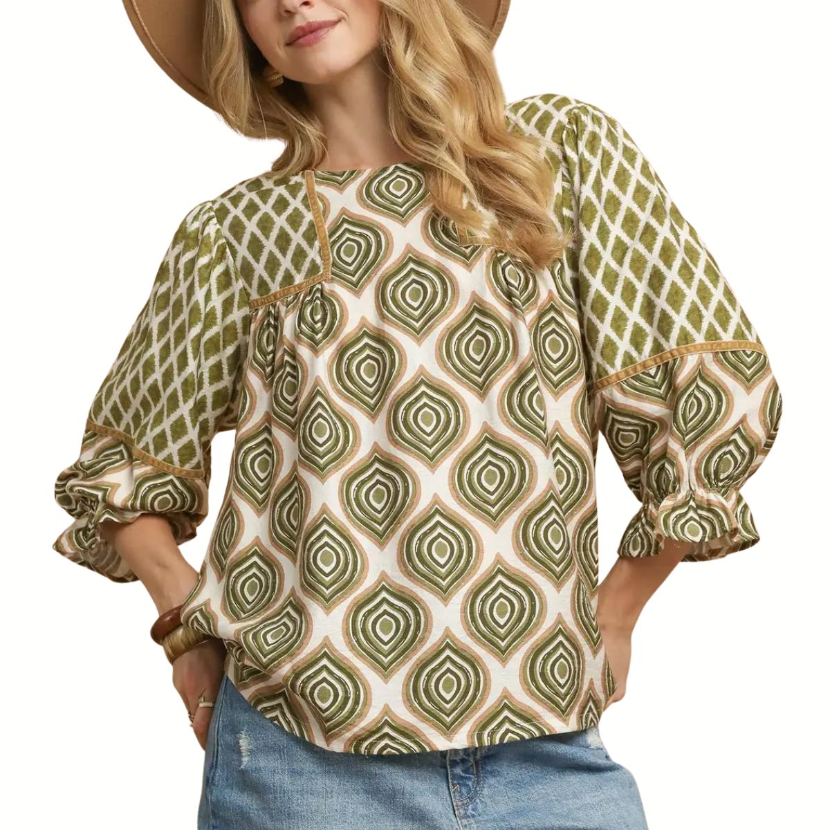 A woman wears the Umgee Retro Geometric Print Top featuring green and beige designs, styled with blue denim shorts and a wide-brimmed hat.