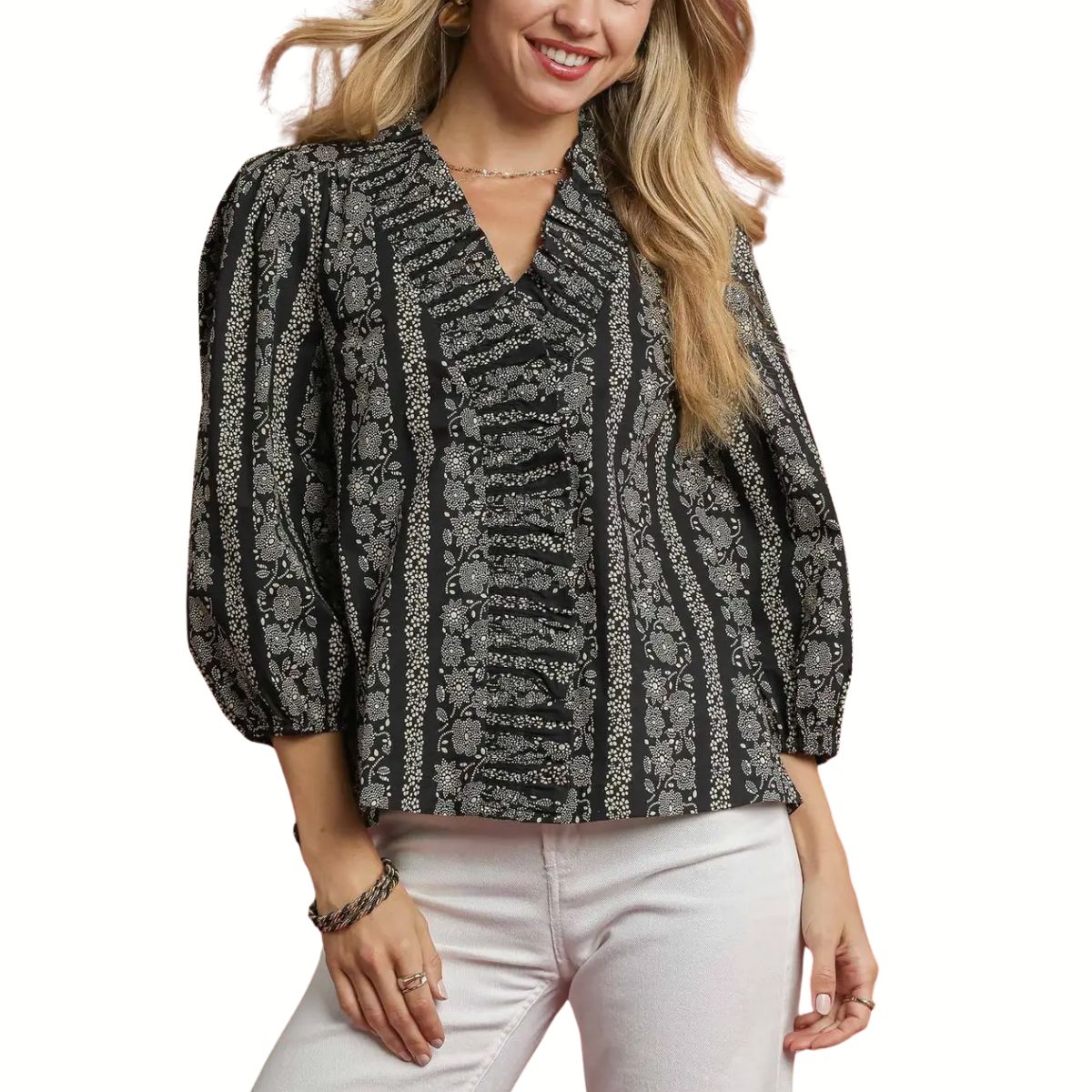 A woman wears the Umgee Abstract Print Ruffle Front Blouse with long sleeves and ruffle details, paired with white pants.