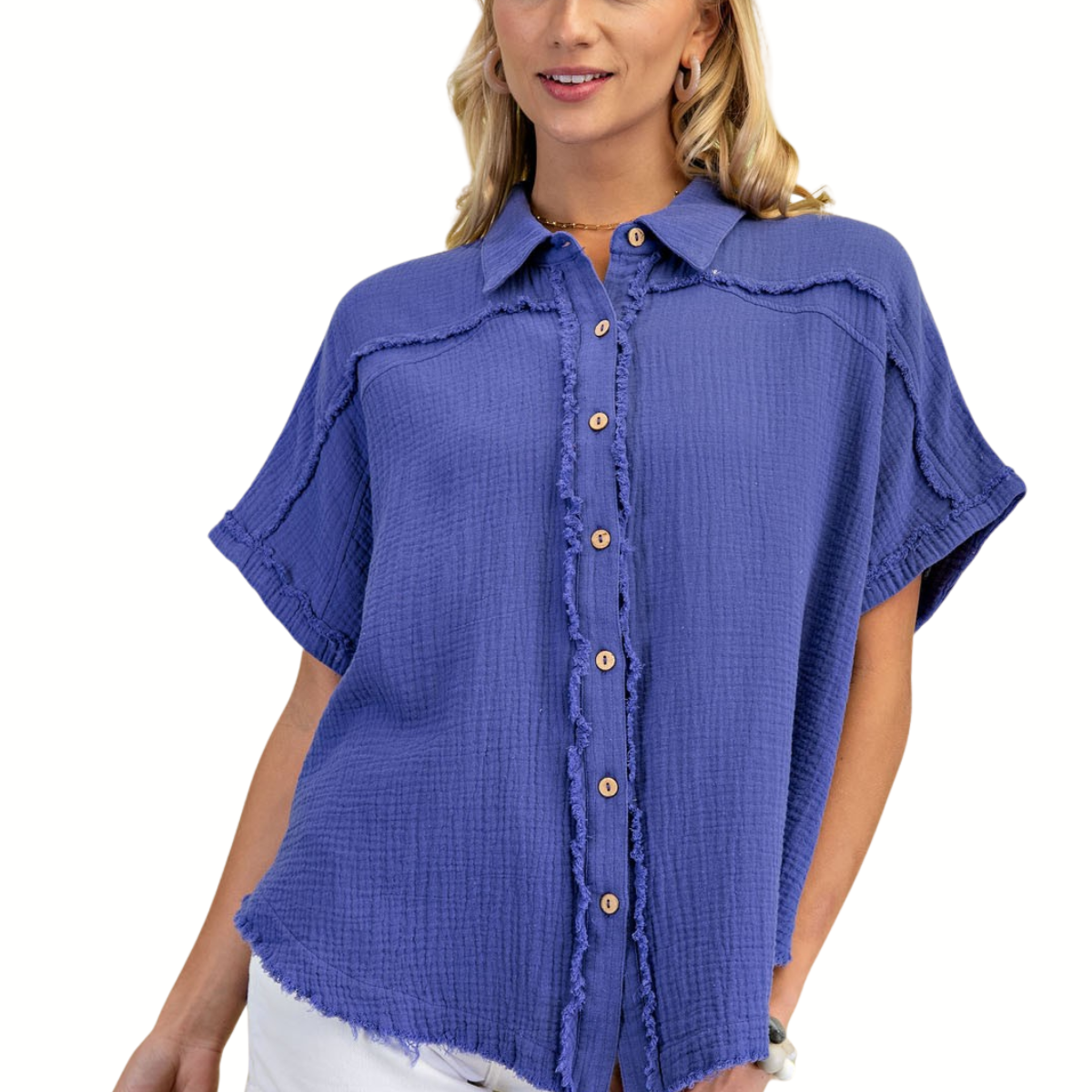 A woman models the Gigio Gauze Button Down Top with Distressed Raw Edge, featuring a loose fit and short sleeves in textured blue fabric, paired with white pants against a white background.