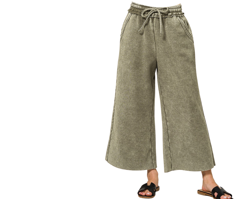 A person stands against a white background wearing Zenana’s Acid Washed Fleece Palazzo Sweatpants in olive green with black sandals.