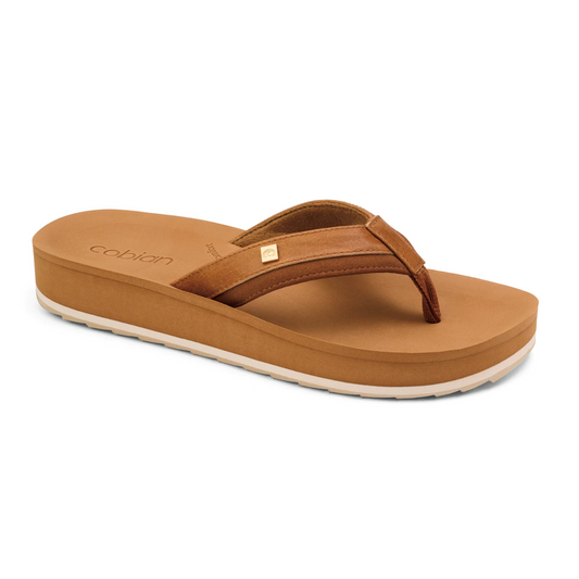 Reya Rise Flip Flops in Tan by COBIAN with a white sole and a small gold emblem on the strap, featuring an anatomical footbed for enhanced cushion and support, displayed against a white background.