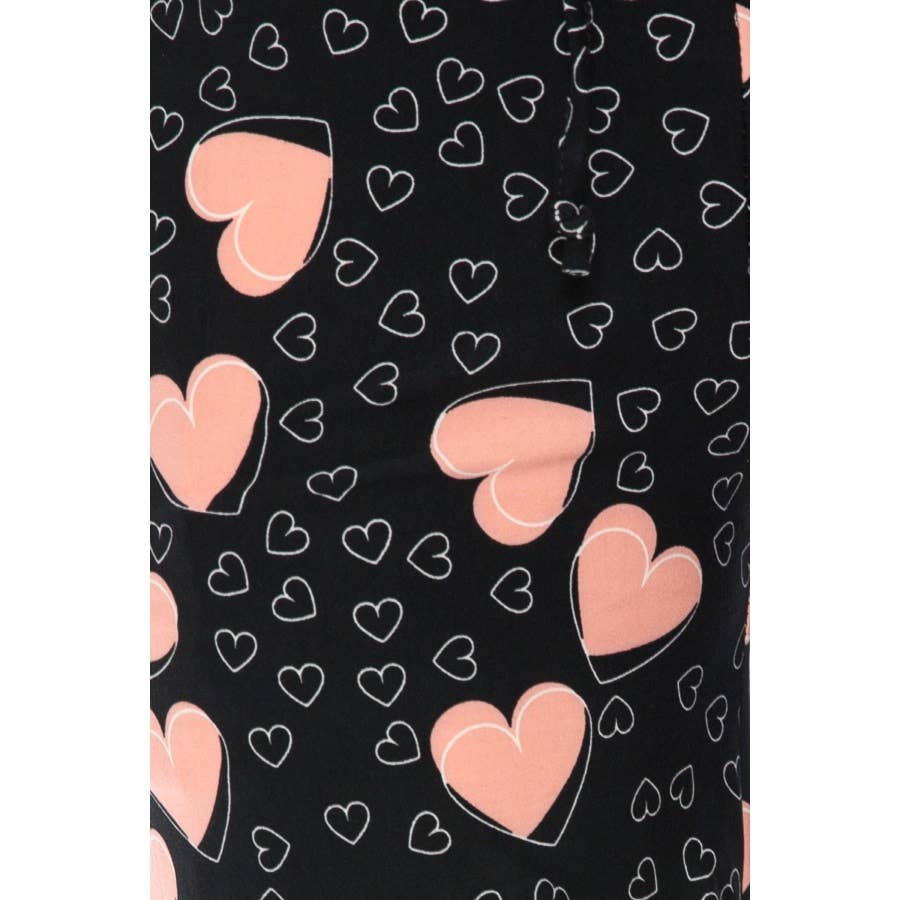 Close-up of Leggings Depotβs Buttery Soft Pajama Pants with an elastic waistband, in black fabric decorated with large pink hearts outlined in white plus small white hearts.