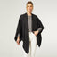 A person wears a black COCO + CARMEN Kiara Lightweight Wrap over a grey top and white pants against a plain light background. This one-size versatile piece brings effortless style and comfort to any outfit.