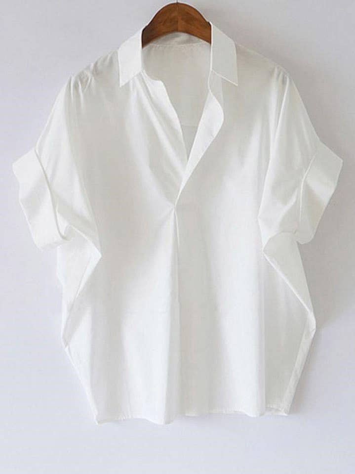 The Rosa Clothing White Relaxed Short Sleeve Blouse hangs on a wooden hanger against a white background, adding a chic touch to any outfit.