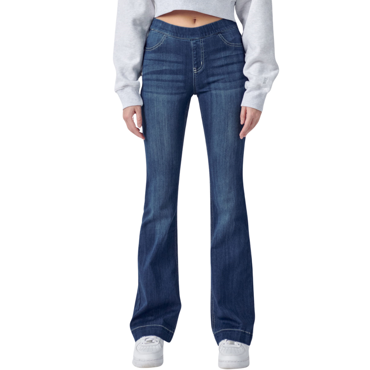 A person wearing Cello Pull On Flare Jeans 33 inch inseam in Dark Denim and white sneakers with a grey crop top, standing against a white background.