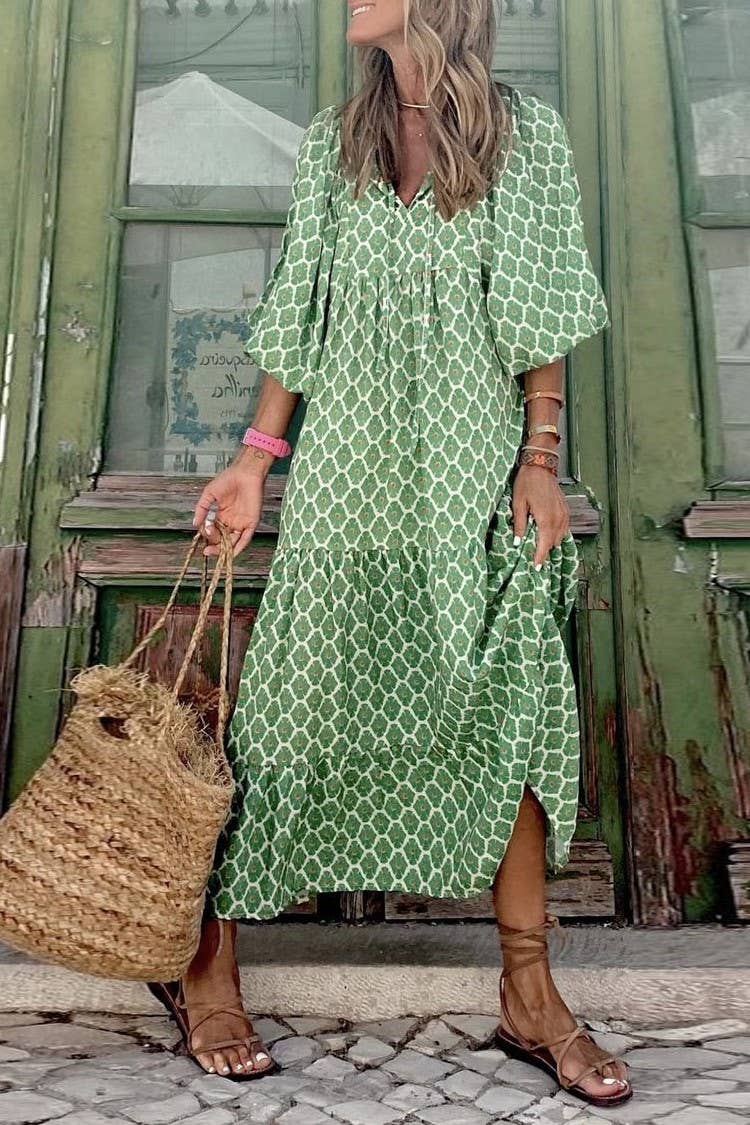 A woman in a Rosa Clothing Bohemian Floral Balloon Sleeves loose flare swing dress stands before an old green door, holding a straw bag and wearing brown sandals—an ideal look for a stylish beach resort getaway.