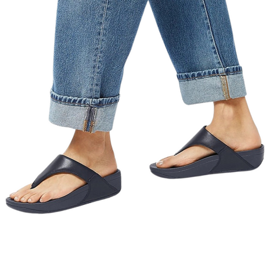 A woman in denim jeans and Lulu Leather flip flop sandals in Deepest Blue by FITFLOP USA LLC.