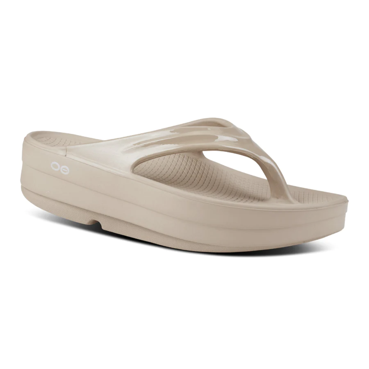 The Women's Oofos OOMEGA THONG Recovery FLIP FLOP in Nomad by OOFOS LLC is a beige platform sandal with a thong-style strap and textured sole, enhanced with OOfoam technology for ultimate comfort, ideal for active recovery.