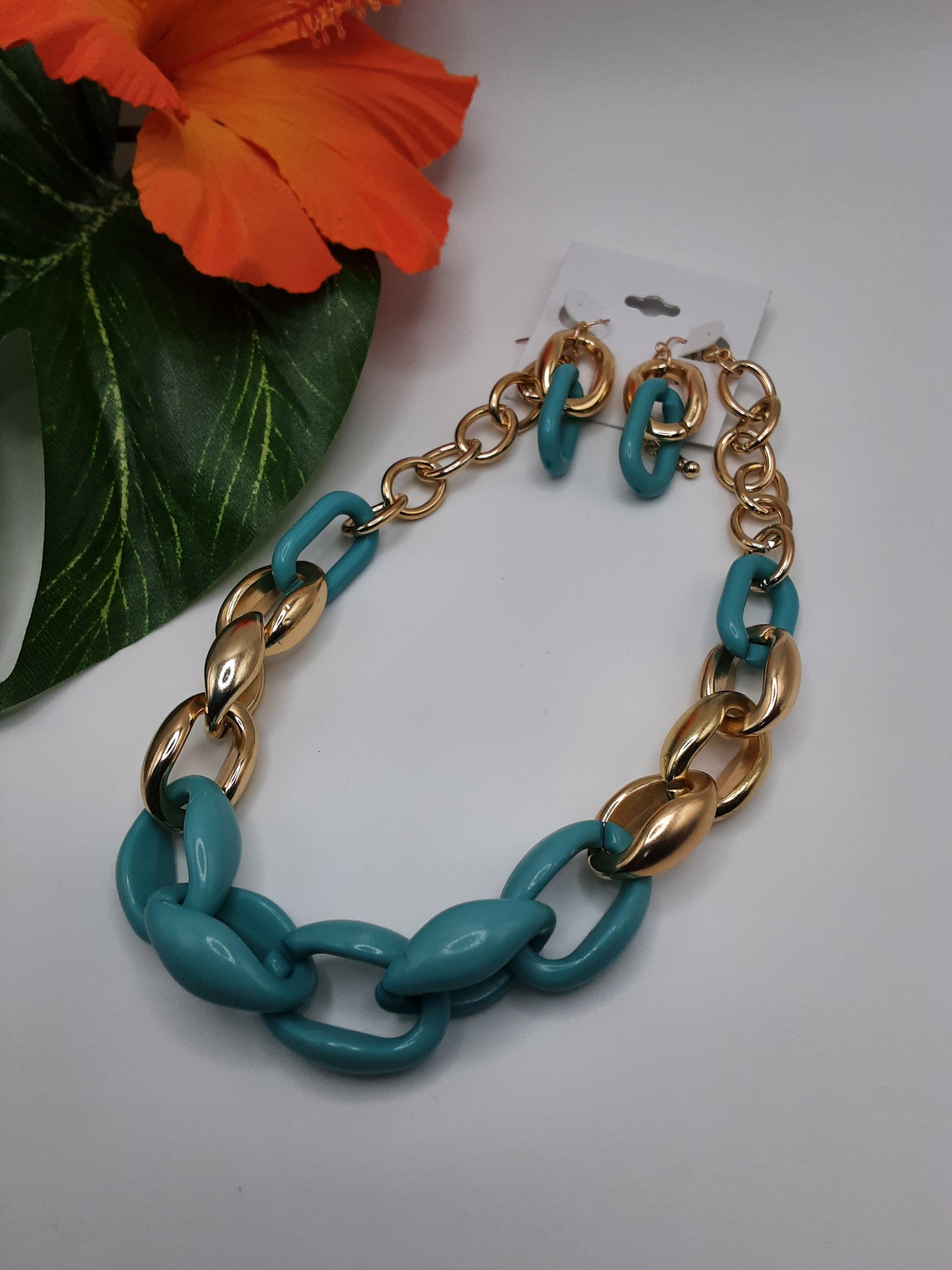A Turquoise Color and Gold Chain Link Short Statement Necklace from SPECIAL EFFECTS, featuring alternating large turquoise and gold oval links, laid out in a display with an orange flower in the background.