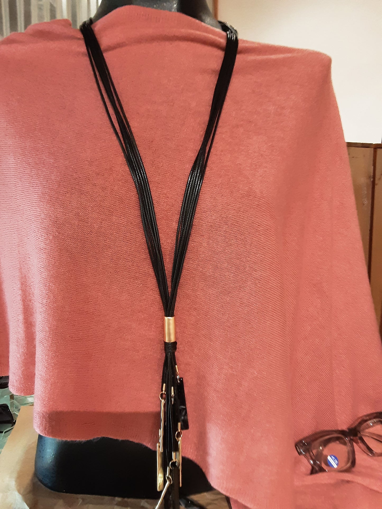 A mannequin dressed in a pink top with the SPECIAL EFFECTS Multi Row Tassel Necklace Set in Black elegantly draped over it; glasses are placed on the side.