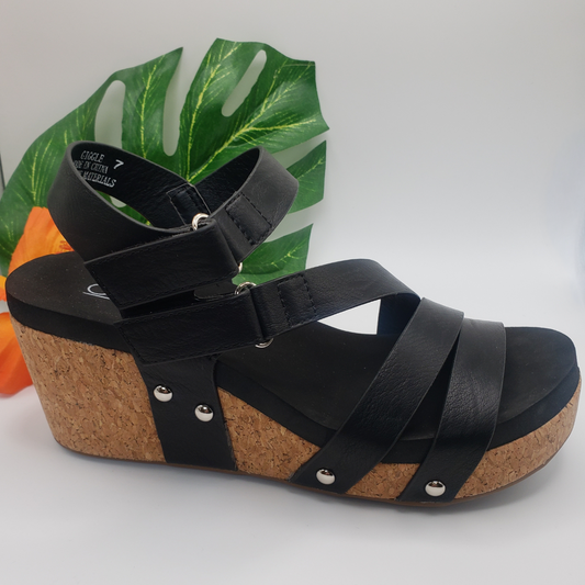 Giggle in Black sandal with velcro closure and Corky's footbed, displayed against a white background with decorative green foliage.