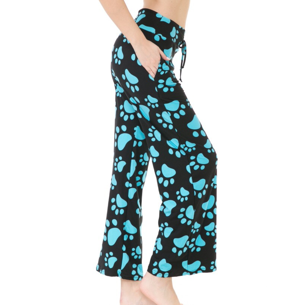 Side view of a person wearing FASHION GO's Buttery Soft Pajama Pants with Drawstring adorned with blue paw print patterns, featuring an elastic waistband and functional pockets. Their right hand is in the pocket, and they are standing barefoot.