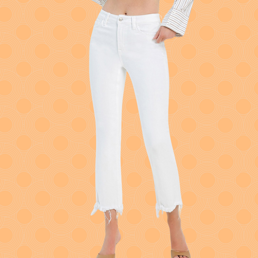 A woman wearing Fashion Go's High Rise Uneven Raw Hem Crop Flare White Jeans - BELLA and brown sandals stands against a peach background with a circular pattern.