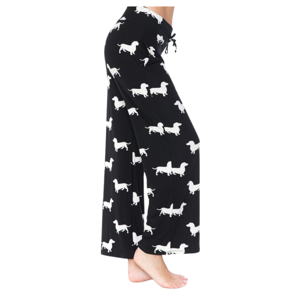 Black pants with a white dachshund pattern, worn by a standing person, only their legs are visible. The buttery soft fabric and elastic waistband of the FASHION GO Buttery Soft Pajama Pants with Drawstring provide ultimate comfort, while the functional pockets add practicality to this adorable design.