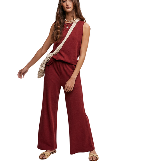 A woman wearing a red sleeveless crew neck Soft Knit Tank top and matching wide-leg Lounge Pant set from FASHION GO, accessorized with a beige shoulder bag and sandals, standing against a plain background.